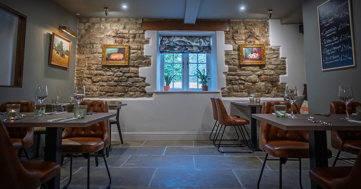 Dining room interior at The Fox at Walton, Wetherby — stone walls, tan leather chairs, tables set for a meal